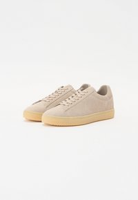 Beige sued sneakers med lav profil, rund tå og snøring. Har et teksturert overdel og kontrastfarget gummisåle.