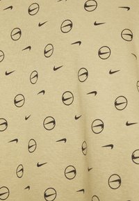 Ljust beige tyg med ett upprepat mönster av svarta basketbollar och Nike-logotyper, som visar en jämn textur och en avslappnad design.