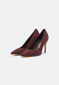 Burgundi zomšo aukšti kulniukai su smailu nosimi ir plonu stiletu. Vidinėje pado dalyje yra balta prekės ženklų etiketė.