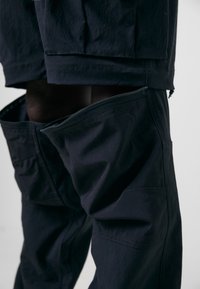Marine Cargo-Hosen mit seitlichen Reißverschlüssen, mehreren Taschen und einer glatten Textur. Das Design umfasst verstärkte Nähte und einen geraden Schnitt.