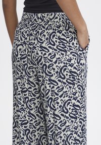 Pantalons navy et crème à motif floral, avec poches latérales et coupe décontractée. Fabriqués dans un tissu léger et texturé.