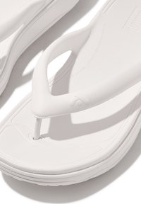 Witte flip-flops met een textuur bovenkant en een gladde zool, met een teensliptont ontwerp en subtiele merktekens aan de zijkant.