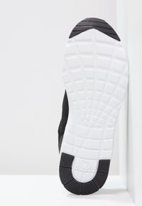 Svart atletisk sul med texturerade mönster. Vit gummimellansula, synlig mönstring för grepp. Mesh-överdel som sträcker sig runt hälen.