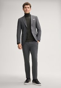 Graues kariertes Anzug mit Revers, schwarzem Rollkragenpullover und schwarzen Sneakers. Glattes Material; taillierte Passform; weißes Taschentuch als Akzent.