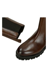 Brązowy skórzany botek za kostkę z elastycznymi panelami po bokach, fakturowaną podeszwą i gładkim wykończeniem, wyposażony w pętelkę ułatwiającą zakładanie.