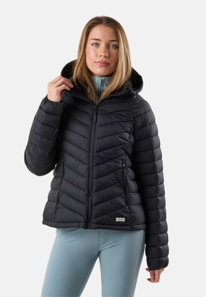 Kvinde iført en sort quiltet hættetrøje med lynlåslommer og lyseblå leggings, stående mod en ensfarvet baggrund.