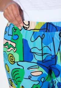 Kleurige, rekbare broeken met een abstract ontwerp in blauw, groen en beige, voorzien van zwarte contouren en een elastische tailleband.