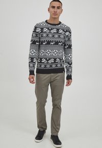 Schwarzer und weißer gestrickter Pullover mit geometrischen Mustern und Schneeflocken, kombiniert mit hellgrauen Hosen und dunklen Sneakers.