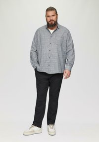 Grijze gemusterde button-up shirt met een borstzak, gecombineerd met zwarte broeken en witte sneakers. Simpel, casual ontwerp met een relaxte pasvorm.