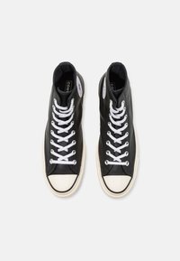 Sneakers alte nere in pelle con lacci bianchi, punta in gomma bianca e dettaglio con logo a lato. Suole piatte e texture liscia.