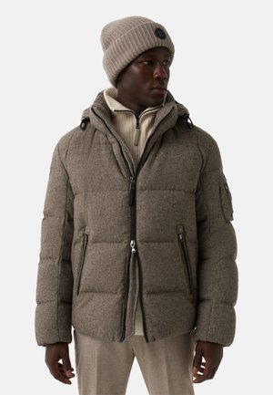 Bruin pufferjack met een gestructureerde afwerking, rits aan de voorkant, capuchon en zijzakken. Draagt een lichtgekleurde trui en een bijpassende gebreide muts.