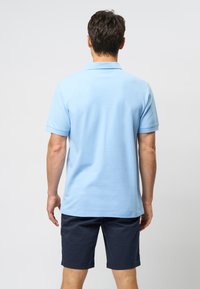 Light blue polo shirt with short sleeves and a textured fabric design, paired with dark navy shorts, displayed from the back.