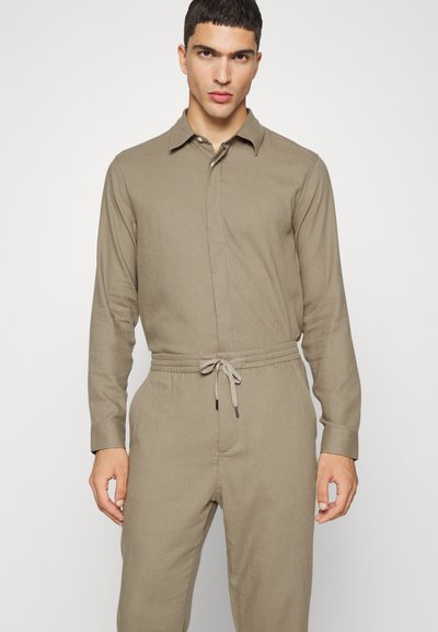 Jardineiro bege com gola, mangas longas, fecho frontal com botões, cintura com cordão e textura suave.