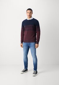 Suéter de hombre en tono navy y burdeos, tejido texturizado con rayas horizontales. Combinado con jeans de color azul claro y zapatillas negras de caña alta.
