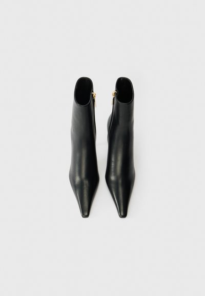 Botas de cuero negras hasta el tobillo con punta afilada, diseño elegante, textura suave y detalles de cremallera dorada en el lado exterior.