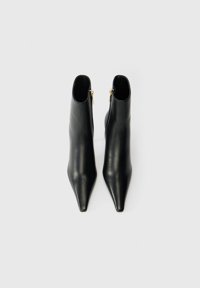 Svarta läderstövlar anklar med spetsig tå, slank design, slät yta och guldzippar på utsidan.