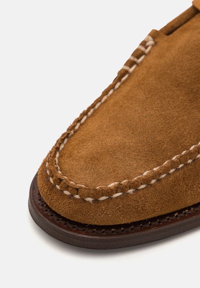 Mocassino in suede marrone con punta chiusa, caratterizzato da cuciture bianche a contrasto attorno al bordo e una suola testurizzata di colore marrone scuro.