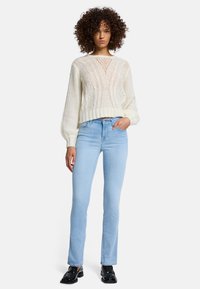 Kremowy sweter dzianinowy z plecionymi wzorami, z dekoltem w kształcie litery V i bufiastymi rękawami, w połączeniu z jasnoniebieskimi dopasowanymi dżinsami i czarnymi loafersami.