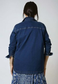 Dark blue denim jacket with long sleeves and buttoned cuffs. Features a straight cut and a smooth texture, visible stitching along the seams.