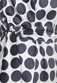 Robe en satin avec de grands pois marins sur fond blanc, présentant un détail de taille nouée et une texture lisse.