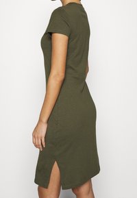 Olivkowa sukienka t-shirtowa, z krótkimi rękawami, okrągłym dekoltem, lekko dopasowany kształt z bocznymi rozcięciami, gładka tkanina bawełniana.