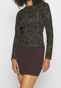 Leopardmönstrad topp i mörkbrun och svart, med långa ärmar och en figurnära design, i kombination med en ribbad brun kjol.