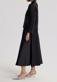 Conjunto de tela negra que incluye una chaqueta corta y una falda larga. Tacones plateados metálicos con punta puntiaguda y correas en el tobillo. Textura suave, diseño sencillo.