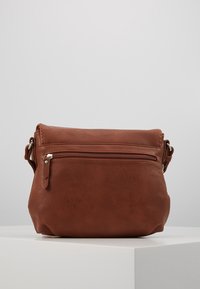 Brun læder crossbody taske med en lynlåslomme foran, rund form og justerbar strop. Glat tekstur med minimalt hardware.