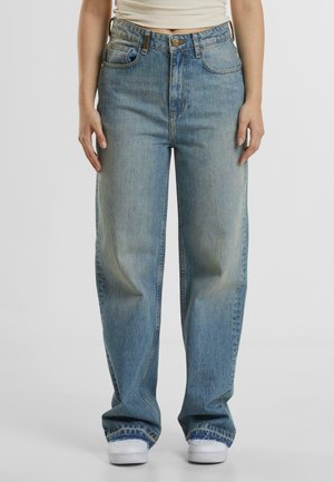 Light blue denim wide-leg jeans with a high waistband, five pockets, and visible stitching details, paired with white sneakers.