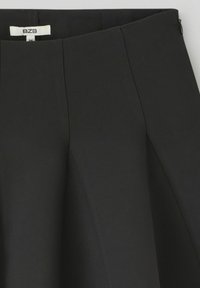 Jupe noire avec un design structuré, des plis et une texture lisse. Comprend une fermeture éclair cachée et une taille étiquetée.