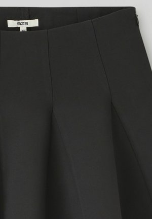 Jupe noire avec un design structuré, des plis et une texture lisse. Comprend une fermeture éclair cachée et une taille étiquetée.