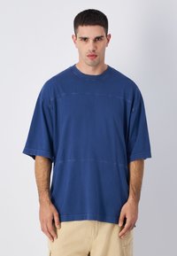 Niebieska bawełniana, oversize koszulka z krótkim rękawem, z zaokrąglonym dekoltem i poziomym szwem. Gładka faktura z luźnym krojem.