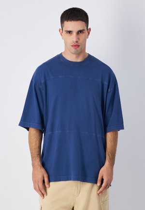 Blauwe katoenen oversized t-shirt met korte mouwen, een ronde halslijn en horizontale naaddetails. Soepele textuur met een relaxte pasvorm.