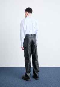 Svarte lær cargo-bukser med avslappet passform, med to side lommer. Modellen har på seg en lyseblå stripete skjorte med knapper.