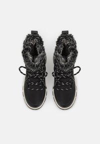 Svarte vanntette støvler med faux fur-fôr, med svart og hvitt mønstrede snører og en solid hvit såle. Ankellengde design.