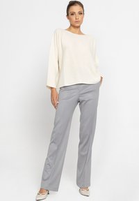 Kremowy sweter z dzianiny z szerokimi rękawami, zestawiony z jasnoszarymi spodniami w kant. Model nosi beżowe buty na szpilkach w kształcie szpicy. Ogólny prosty design.