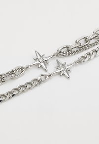 Collier en chaîne argentée avec des maillons entrelacés et des accents en forme d'étoile ornés de pierres claires, mettant en valeur un mélange de surfaces lisses et texturées.