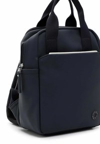 Černý batoh vyrobený z odolného materiálu, s dvěma horními madly, přední kapsou na zip a logem na jedné straně.