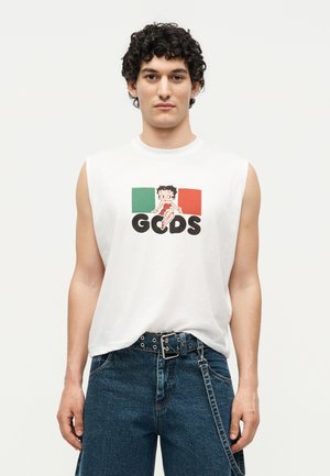 Jeune homme portant un t-shirt blanc sans manches avec le drapeau italien, un motif Betty Boop et des lettres GCDS noires, associé à un jean bleu et une ceinture.