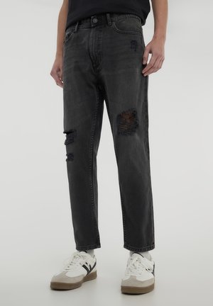 Jeans in denim nero con una vestibilità rilassata, caratterizzati da dettagli strappati, toppe sfilacciate sulle ginocchia e un classico design a cinque tasche.