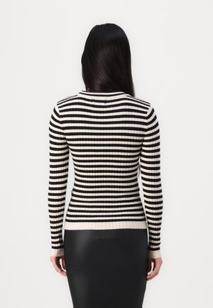 Vrouw met lang, donker haar, gekleed in een zwart-witte horizontaal gestreepte ribgebreide trui en een zwarte rok, gezien vanuit de rug.