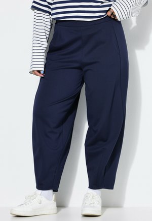 Personne portant un pantalon large bleu marine, des chaussettes blanches, des baskets blanches et un t-shirt à manches longues rayé avec des rayures horizontales bleu marine et blanches.