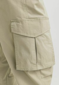 Beige Cargohosen mit großen Seitentaschen, aus strapazierfähigem Stoff. Merkmale sind genähte Nähte und ein lockerer Schnitt.