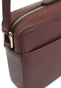 Sac à main en cuir marron avec une finition texturée, fermeture éclair dorée, forme rectangulaire et une seule sangle réglable. Présente des détails de couture visibles.