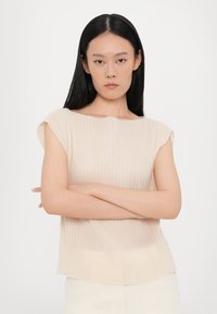 Beige ribbed knit top with a round neckline and short sleeves, featuring a slightly sheer texture and a relaxed fit.