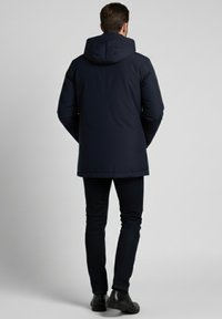 Abrigo acolchado azul marino oscuro con capucha, de corte recto, detalles de costura sutiles y textura de tela suave. Combina con pantalones y zapatos oscuros.