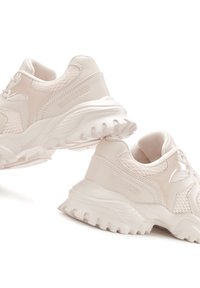 Chaussures de sport rose clair avec une tige texturée, des accents en mesh et une semelle épaisse dotée de crampons prononcés. Logo affiché sur le côté.