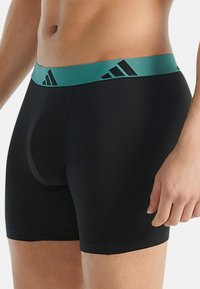 Zwarte boxershorts met een turquoise elastische tailleband met zwarte logo-details. Glad materiaal met een fitted ontwerp.