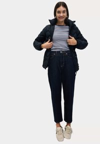 Černá prošívaná bunda přes námořnickou a bílou pruhovanou košili, v kombinaci s vysokým pasem tmavými džínami a béžovými teniskami.