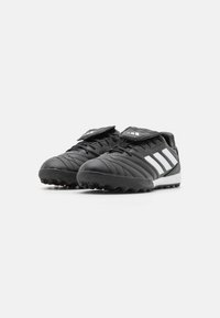 Scarpe sportive nere con accenti bianchi, caratterizzate da una superficie texturizzata, punta arrotondata e un design a profilo basso. Includono chiusure con lacci e a patta.